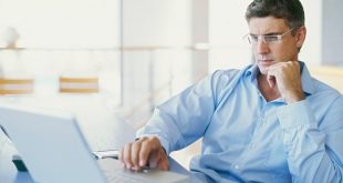 man in blue shirt sitting in front of a laptop in an office